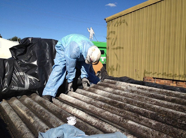 Man removing asbestos roofing material | Featured image for Commercial Demolition Brisbane page Gumdale Demolitions